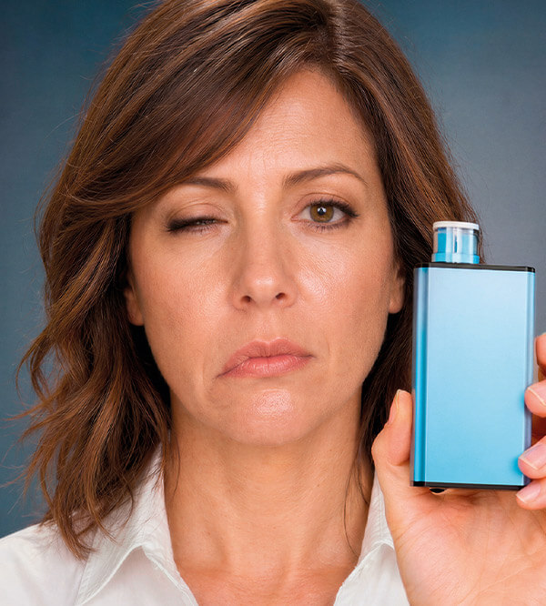 Mujer adulta con un ojo cerrado sosteniendo un vape azul